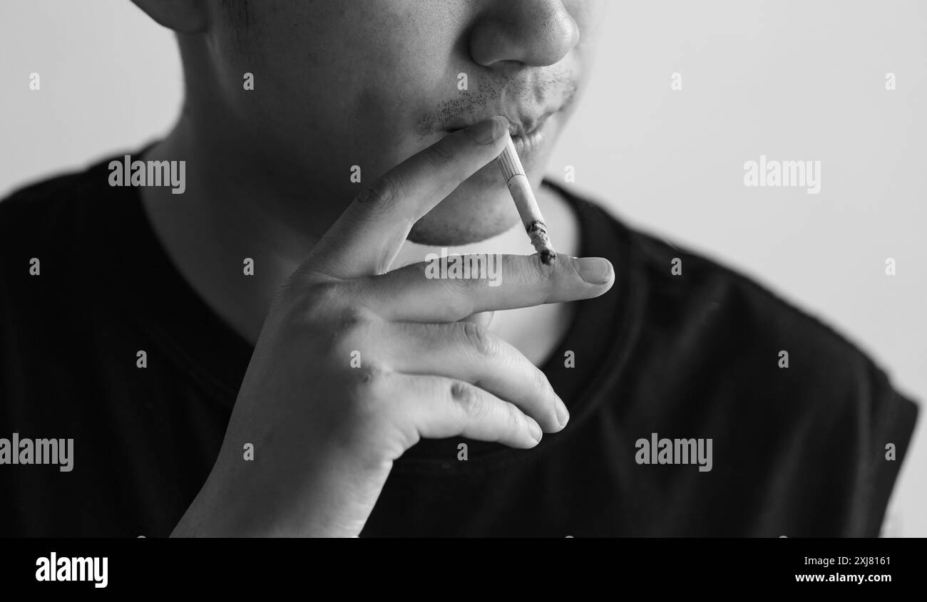 Gros plan jeune homme fumant une cigarette. Fumer la cigarette dans la main d'un jeune homme. Un gars accro à la cigarette. Cigarette dans la bouche de l'homme. Gros plan pho Banque D'Images
