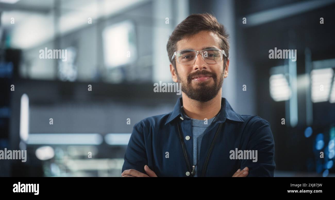 Beau Indien portant des lunettes et une chemise bleu foncé souriant et regardant la caméra. Jeune homme d'Asie du Sud travaillant comme ingénieur ou scientifique dans l'installation de recherche technologique Banque D'Images