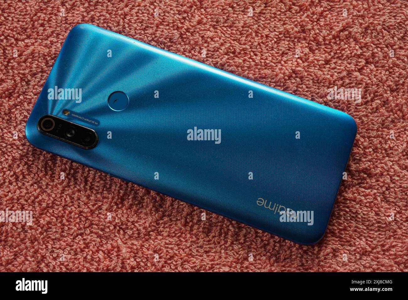 Terengganu, Malaisie - 2 août 2024 : panneau arrière du smartphone realme bleu sur fond rouge. Téléphone milieu de gamme Realme. Banque D'Images