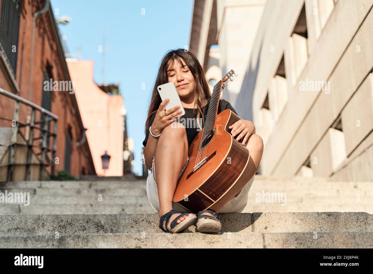 jeune femme brune latina assise avec une guitare tout en utilisant son téléphone intelligent Banque D'Images