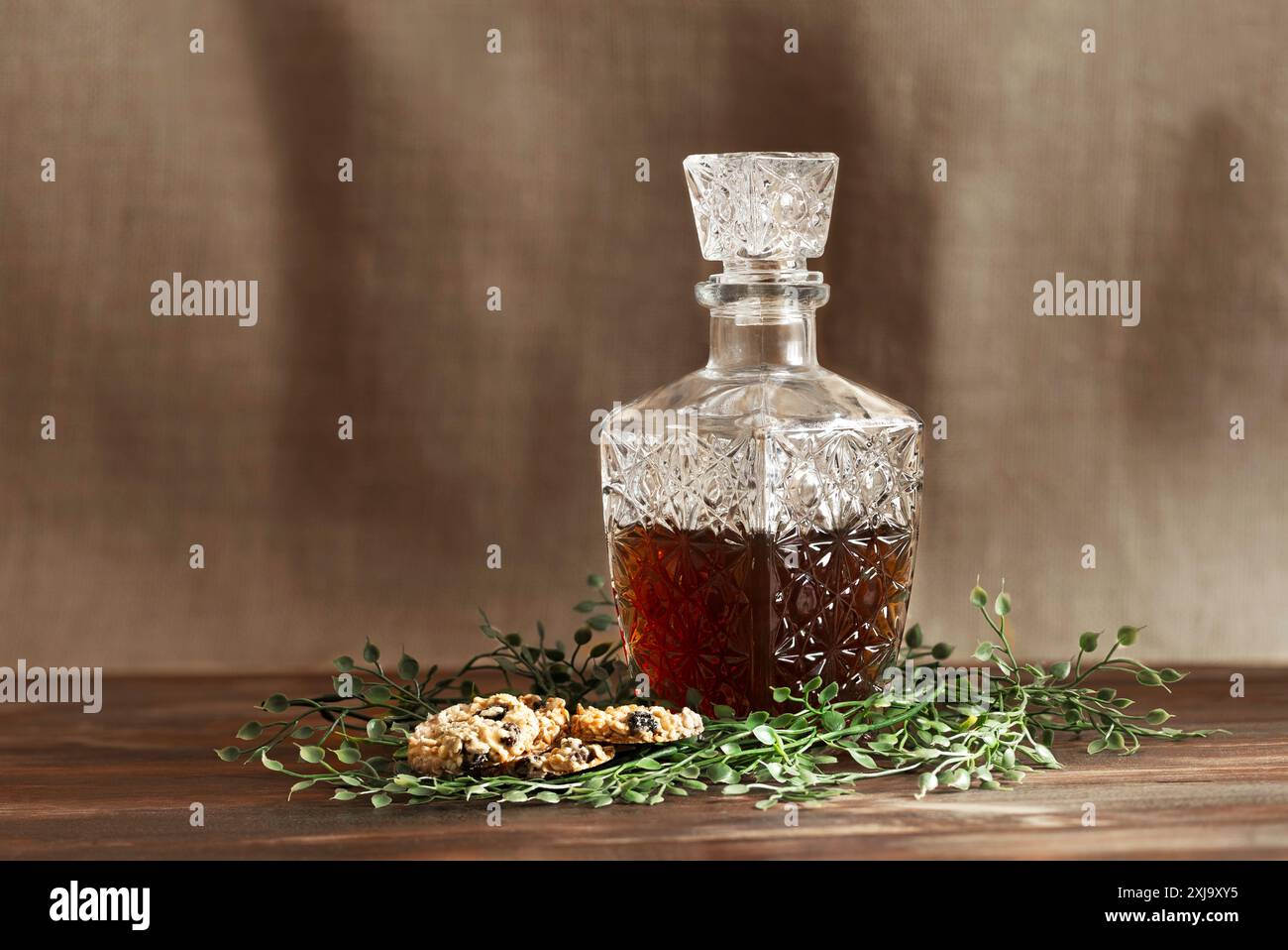 Bouteille de liqueur en verre sculpté avec des biscuits et des branches vertes sur une table en bois et un fond brun. Festivité. Horizontal. Banque D'Images