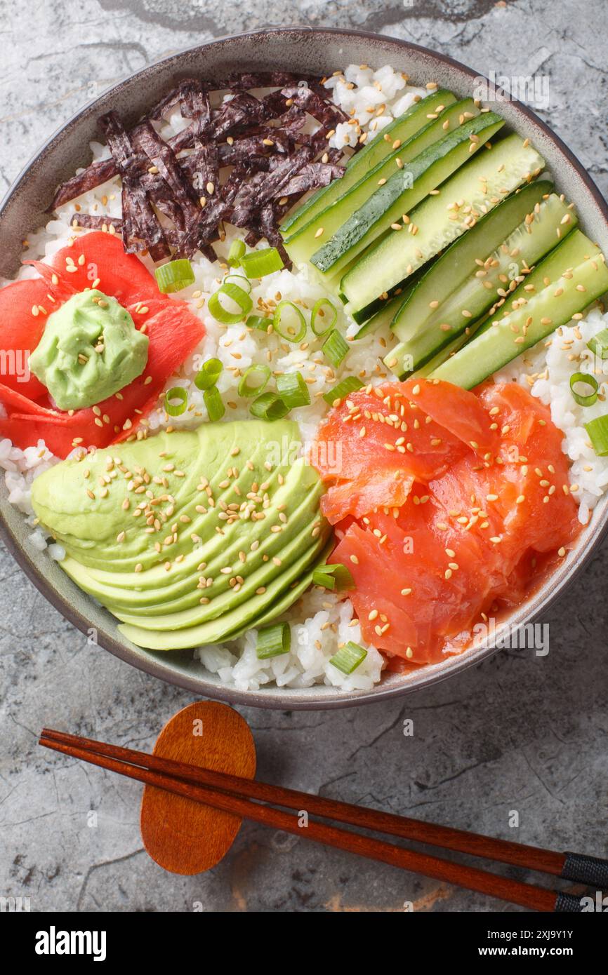 Bol à sushi asiatique avec saumon, riz, avocat, concombre, oignon vert, algues, sésame, gingembre mariné et wasabi gros plan sur la table. Vie supérieure verticale Banque D'Images