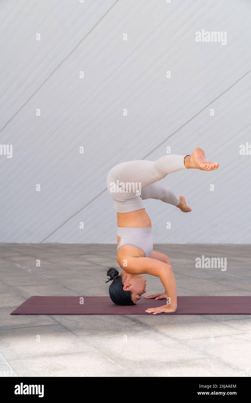 Une femme brune vêtue de vêtements de sport faisant une variation de la pose salamba sirsasana 2 avec les jambes écartées sur les côtés. Banque D'Images