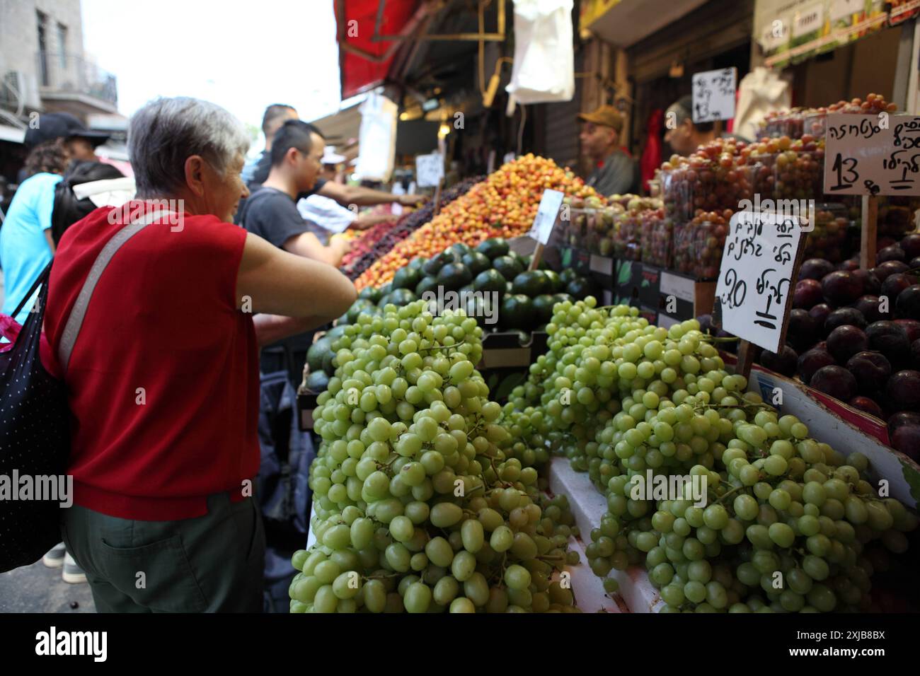 Femme élégante israélienne portant des vêtements d'été cherche à acheter des fruits sur un stand de marché Machane Yehuda, raisins, prunes, avocats et cerises sont vendus. Banque D'Images