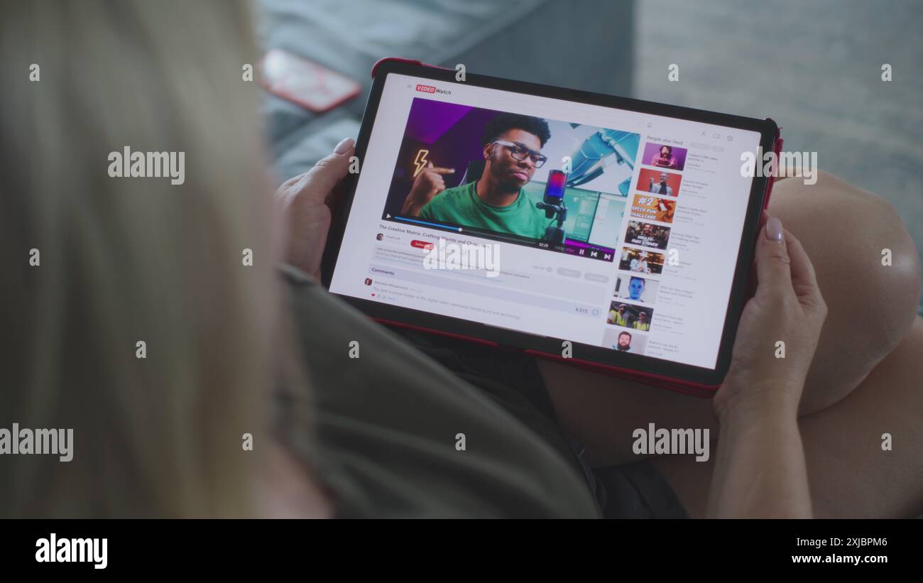 Femme caucasienne regarde la vidéo éducative de blogueur sur la modélisation 3D en utilisant la tablette ordinateur tout en étant allongé sur le canapé. L'écran de la tablette affiche l'interface du site Web d'hébergement vidéo avec le contenu vidéo. Gros plan. Banque D'Images