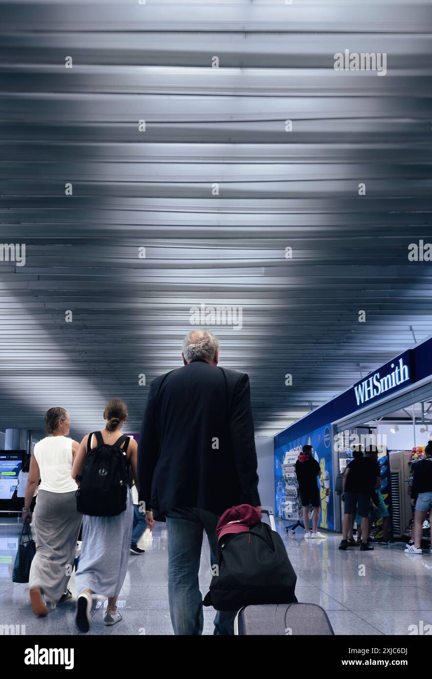 Palma, Espagne - 11 juillet 2024 : vue arrière de voyageurs marchant à travers un terminal d'aéroport, avec un magasin WHSmith visible sur le côté et un homme tirant une valise, soulignant l'environnement occupé de l'aéroport Banque D'Images