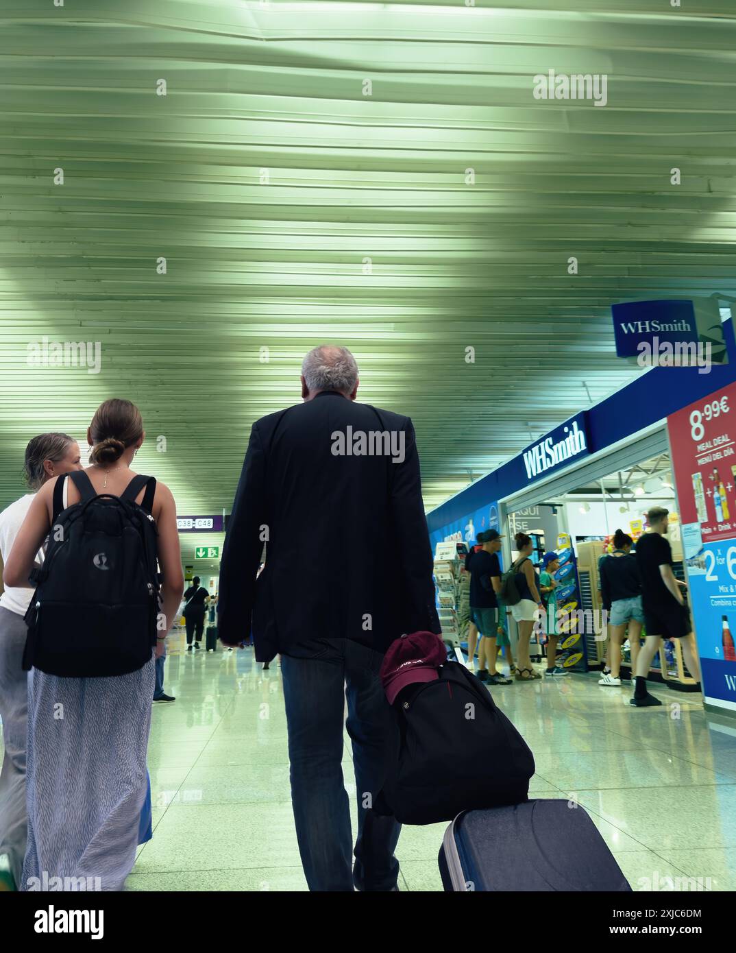Palma, Espagne - 11 juillet 2024 : voyageurs marchant dans un terminal d'aéroport avec un magasin WHSmith sur la droite, avec un homme tirant une valise dans un environnement animé. Banque D'Images