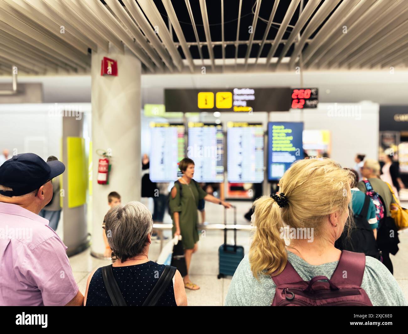 Palma, Espagne - 11 juillet 2024 : les passagers d'un terminal d'aéroport vérifient les informations de vol sur des écrans numériques, en mettant l'accent sur une femme tenant une valise et d'autres voyageurs à proximité. Banque D'Images