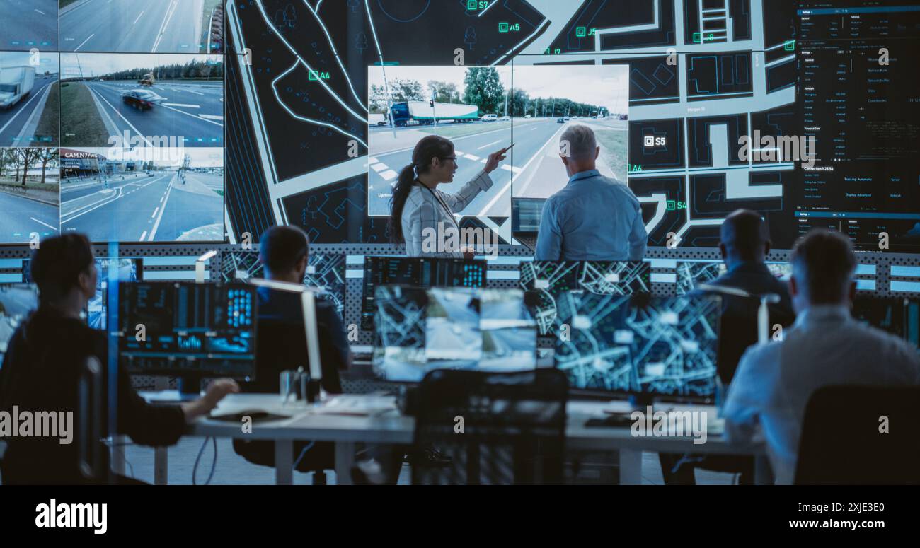 Équipe de développeurs de logiciels, ingénieurs et scientifiques de données travaillant dans une société de technologie logistique moderne. Homme et femme discutant devant un écran avec des séquences de vidéosurveillance Banque D'Images
