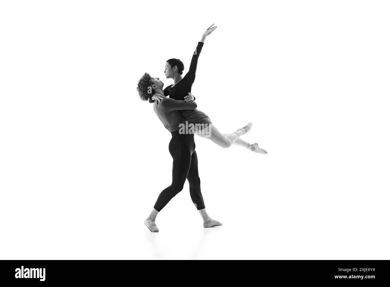 Les danseurs de ballet en duo concentrés et apaisés se déplacent élégamment pendant la session d'entraînement sur fond blanc de studio. Filtre noir et blanc. Banque D'Images