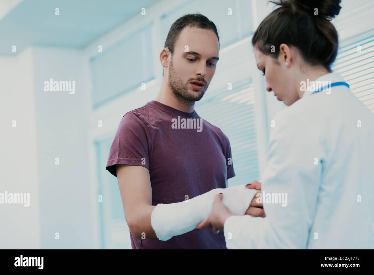 Le médecin attentionné examine un bras cassé dans un hôpital, discutant des options de traitement avec empathie. Le patient écoute attentivement, soulignant la confiance dans la guérison Banque D'Images