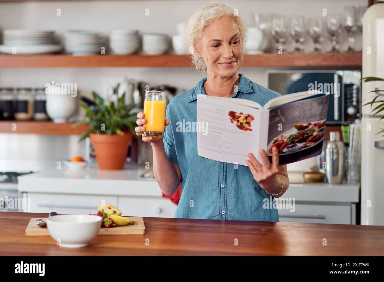 Femme mature, jus et livre de recettes pour l'alimentation, les ingrédients et lire pour les instructions dans la cuisine. Vegan, boisson à l'orange et cuisine pour la nourriture à la maison Banque D'Images