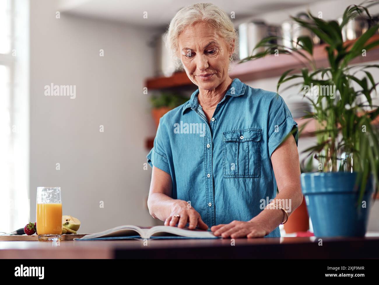 Femme mature, lire et livre de recettes pour le repas, les ingrédients et apprendre pour les instructions dans la cuisine. Vegan, orange et cuisine pour la nourriture à la maison, femelle Banque D'Images