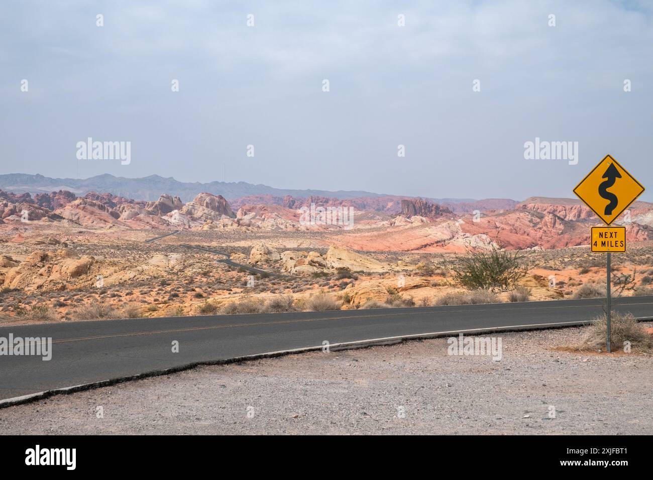 Un panneau jaune avec une courbe sur elle est sur une route dans le désert. La route est vide et le ciel est nuageux Banque D'Images