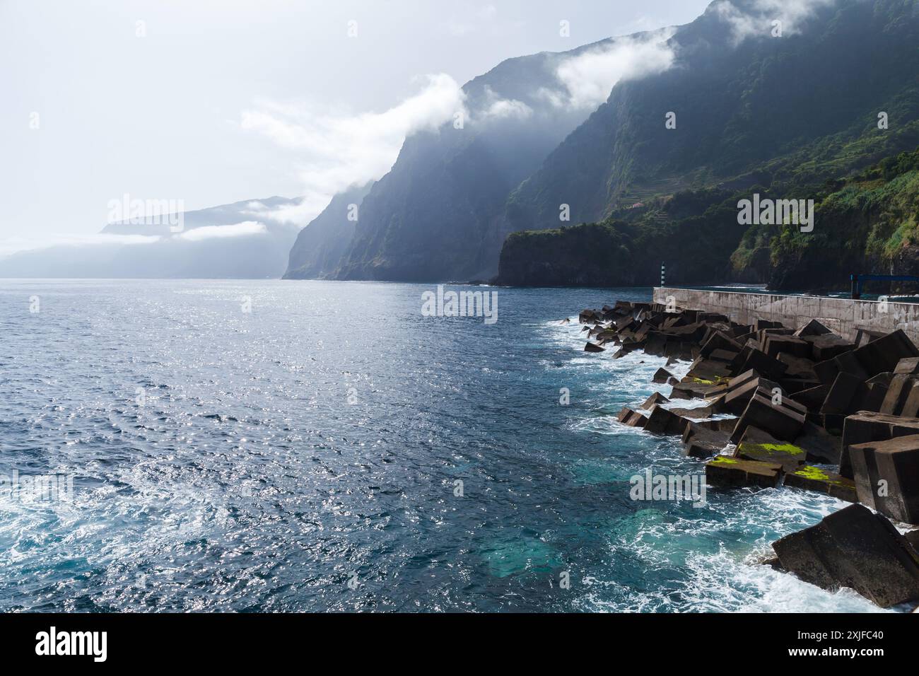Paysage côtier de l'île de Madère, Portugal. Brise-lames en pierre avec poteau de phare blanc vert à l'entrée du port de Seixal Banque D'Images