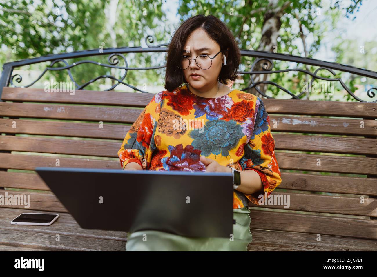 Femme professionnelle asiatique mène une vidéoconférence tendue à distance dans le parc. Femme asiatique en colère participant à des appels vidéo occupés sur son ordinateur portable pendant sitti Banque D'Images