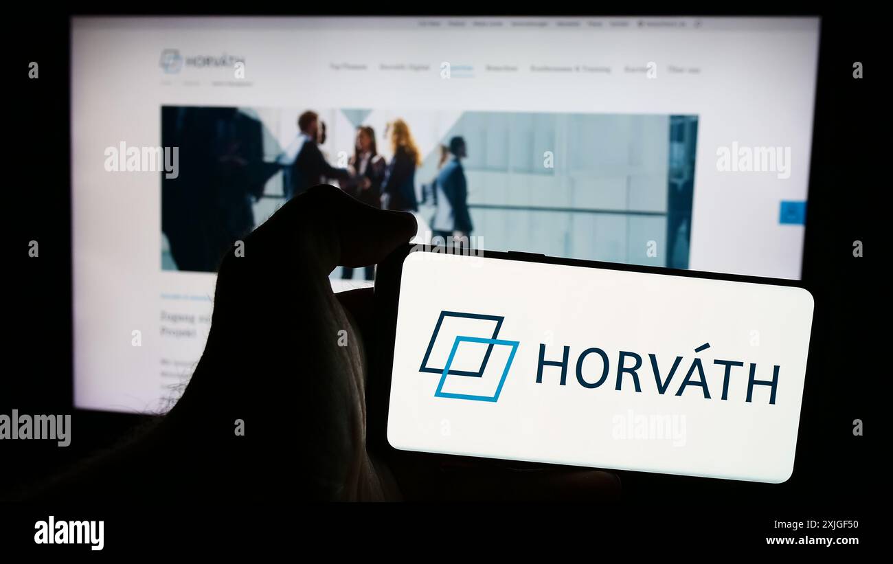 Personne tenant le téléphone portable avec le logo de la société allemande de conseil en gestion Horvath AG en face de la page Web de l'entreprise. Concentrez-vous sur l'affichage du téléphone. Banque D'Images