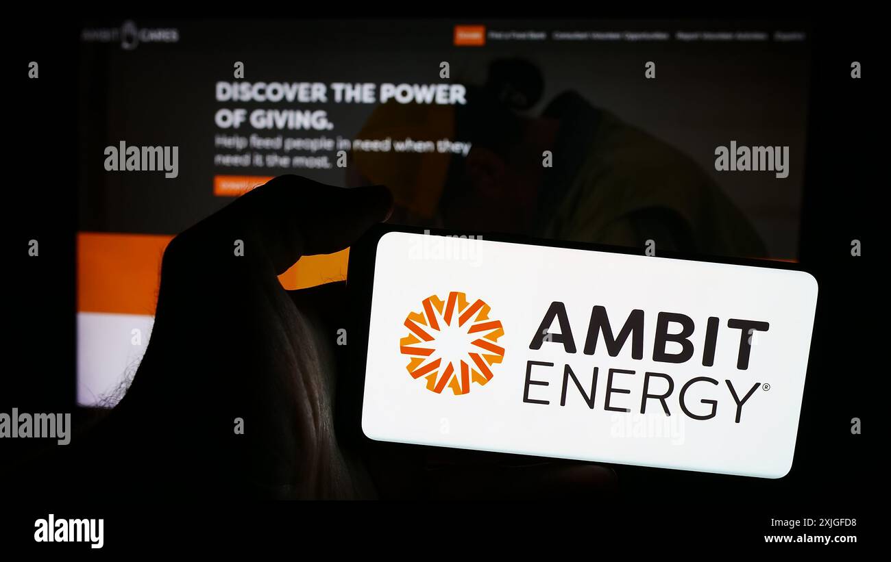 Personne tenant un smartphone avec le logo de la société américaine de marketing multi-niveaux Ambit Energy en face du site Web. Concentrez-vous sur l'affichage du téléphone. Banque D'Images