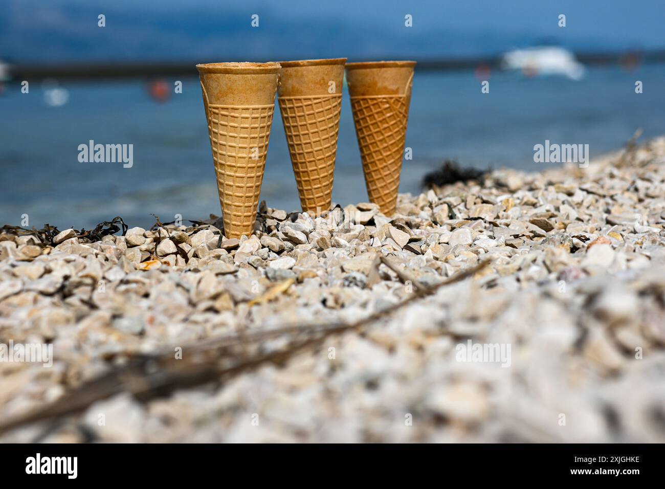 Profitez des vibrations estivales avec des pommes de gaufres de crème glacée vides sur une plage de galets, avec la mer scintillante en toile de fond. Banque D'Images