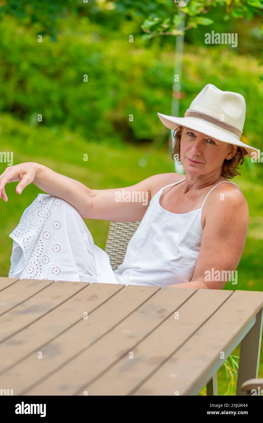 Femme en robe blanche et chapeau relaxant à la table extérieure Banque D'Images