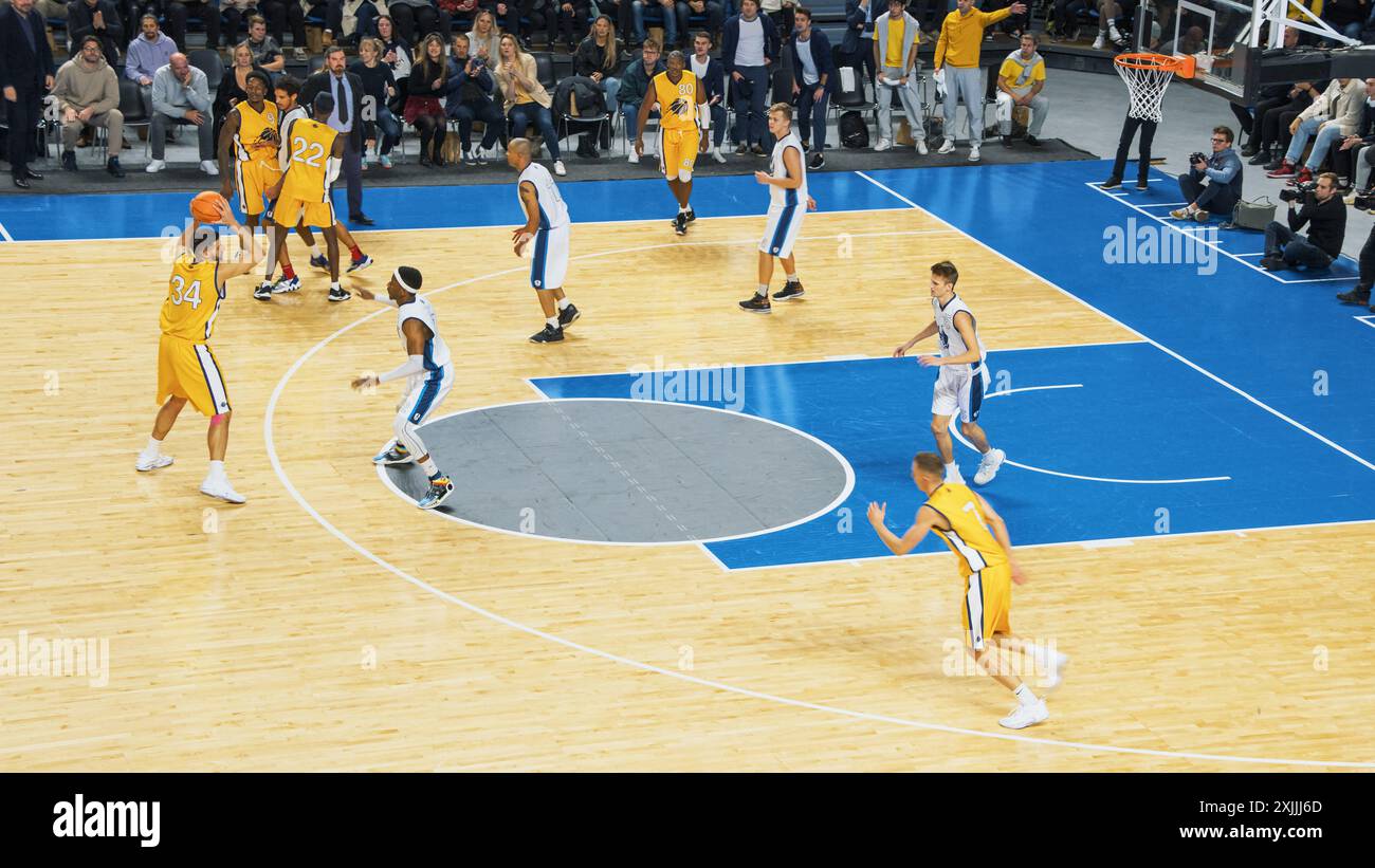 Film de style télévisé du championnat de basket-ball dans une arène. Équipe jaune passant le ballon entre coéquipiers, attaquant visant à marquer un but de deux points à distance. Chaîne sportive. Banque D'Images