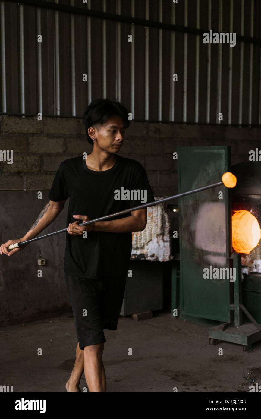 L'homme travaillant avec le verre fondu à l'aide d'une pincette dans une usine de verre Banque D'Images