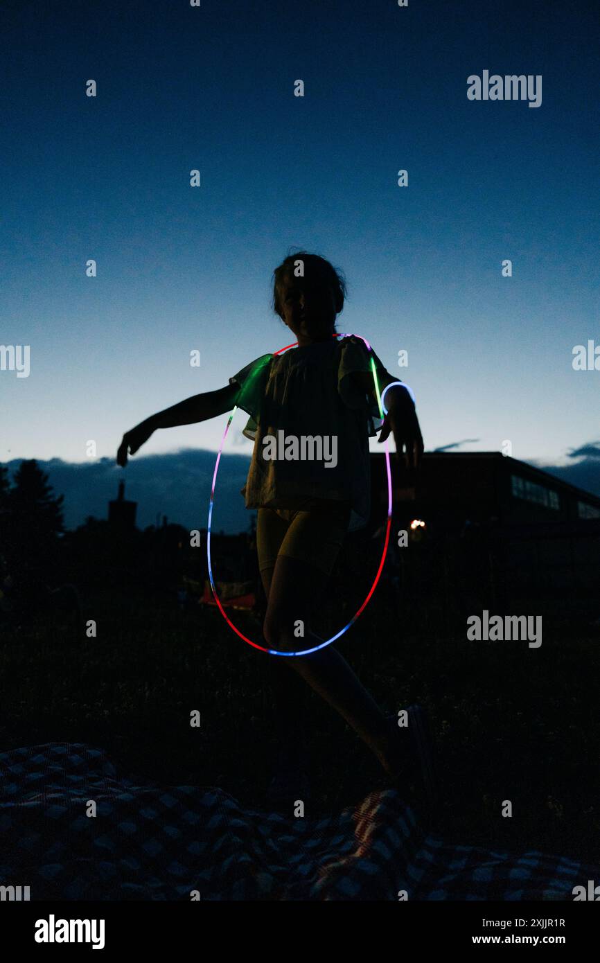 Enfant jouant avec des bâtons phosphorescents dans l'obscurité à l'extérieur Banque D'Images