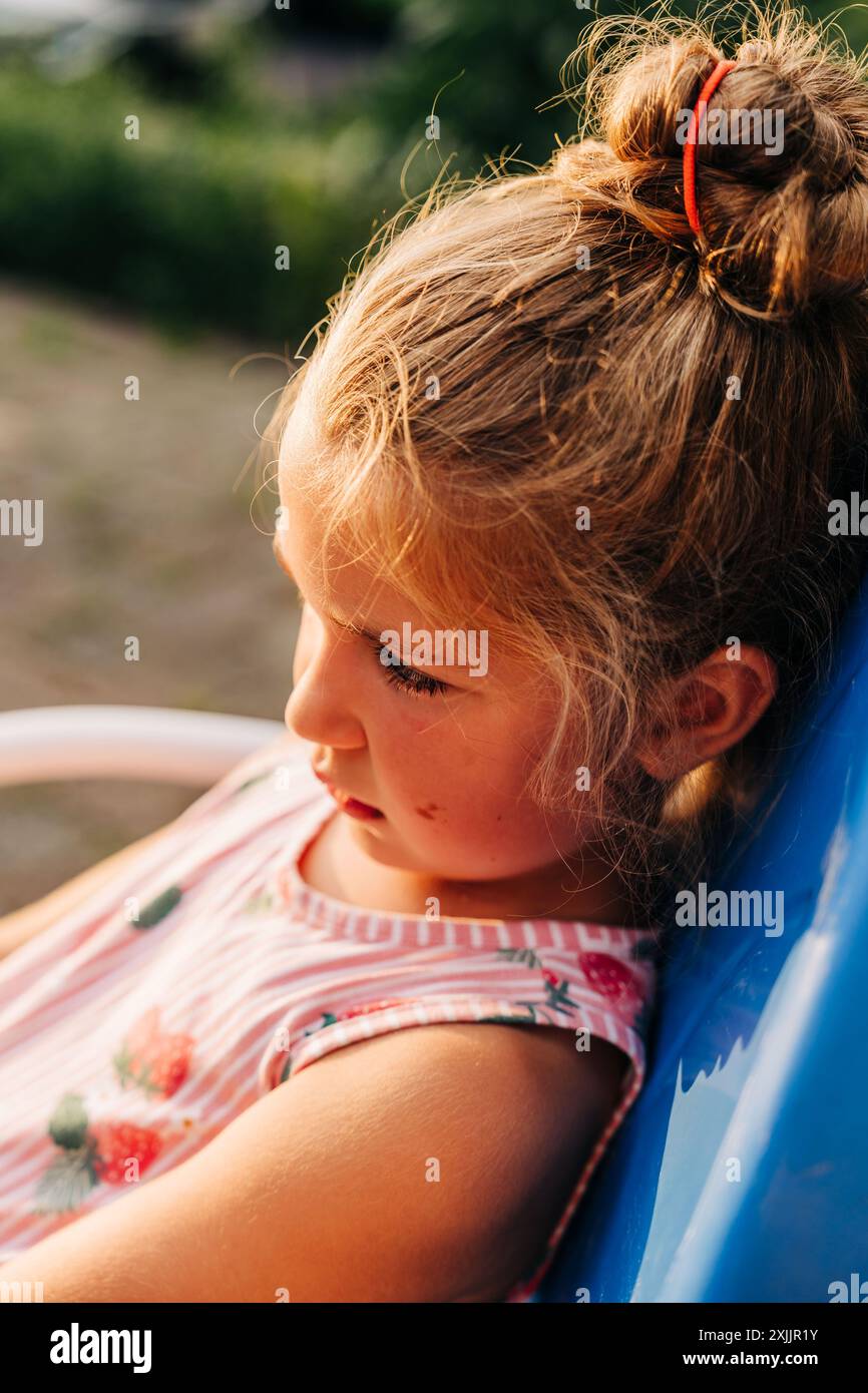 Gros plan d'une fille en robe rayée assise sur une chaise bleue Banque D'Images