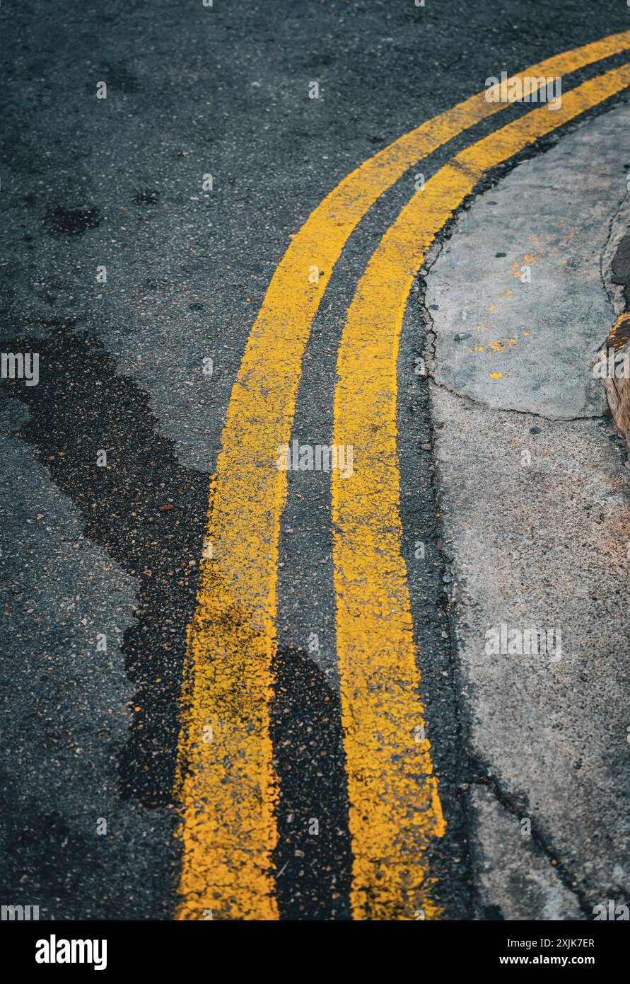 Vue détaillée des doubles lignes de circulation jaunes sur une courbe de route urbaine altérée, signifiant l'absence de stationnement et de division de voie. Banque D'Images