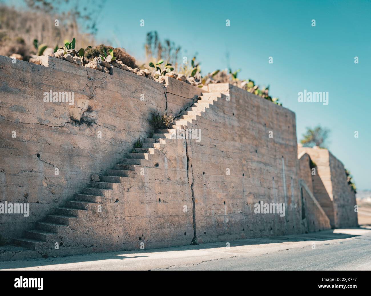 Un escalier en béton dépasse d'un vieux mur de pierre altérée sous un ciel bleu clair. Cadre extérieur minimaliste. Banque D'Images