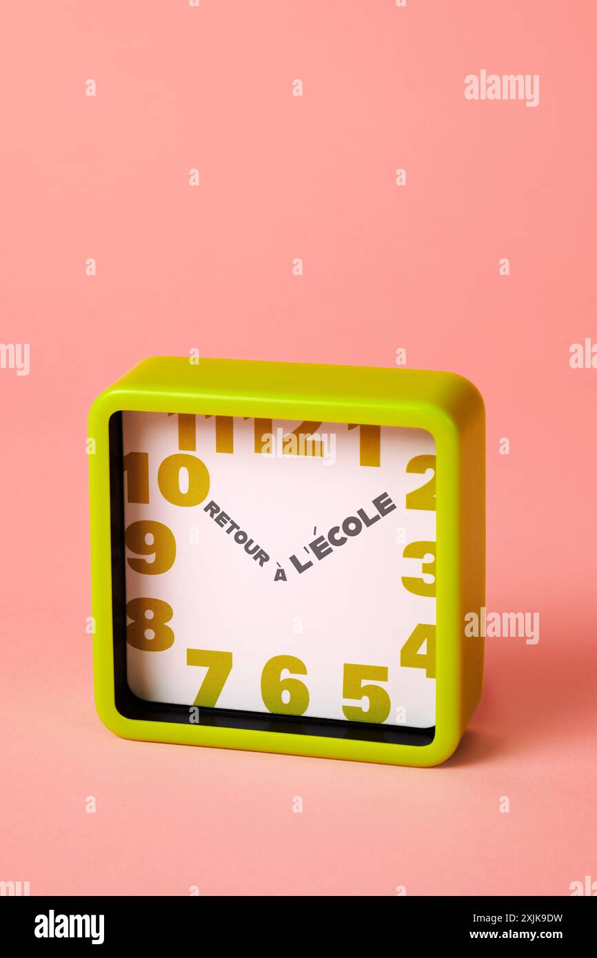 une horloge carrée verte, avec des chiffres verts et le texte de retour à l'école écrit en français au lieu des aiguilles des heures et des minutes, sur un fond rose Banque D'Images