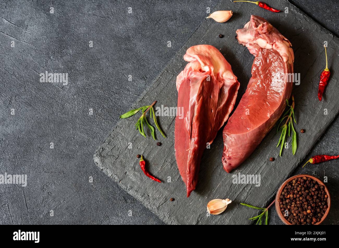 Viande de coeur de bœuf crue sur planche de pierre avec thym et poivrons, abats de bétail Banque D'Images