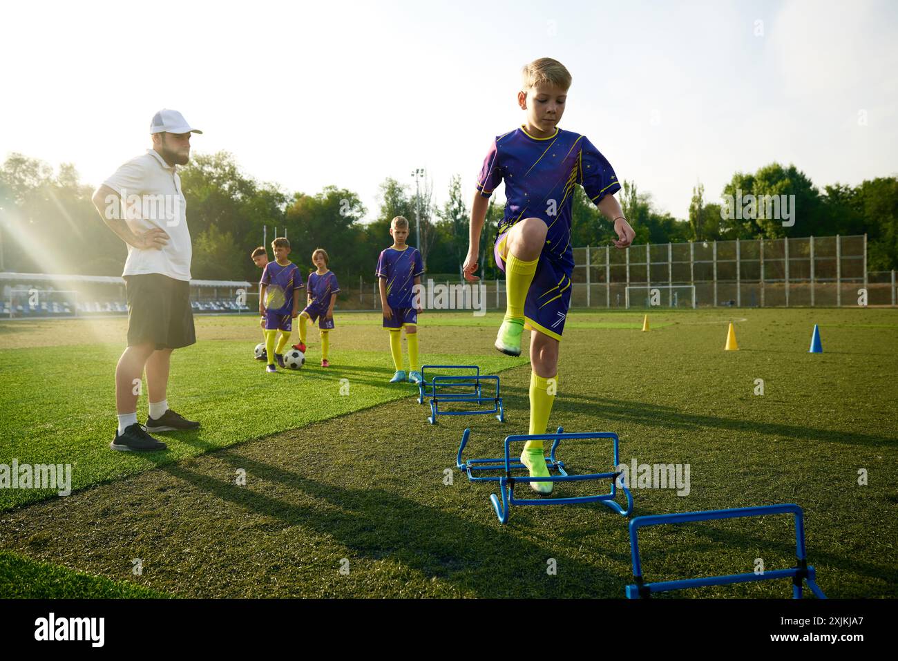 Garçons en uniforme, enfants pratiquant, exercices d'échauffement de pâte sur le sport déposé, sauter par-dessus les obstacles avant le match de football. Observation ciblée de l'entraîneur Banque D'Images