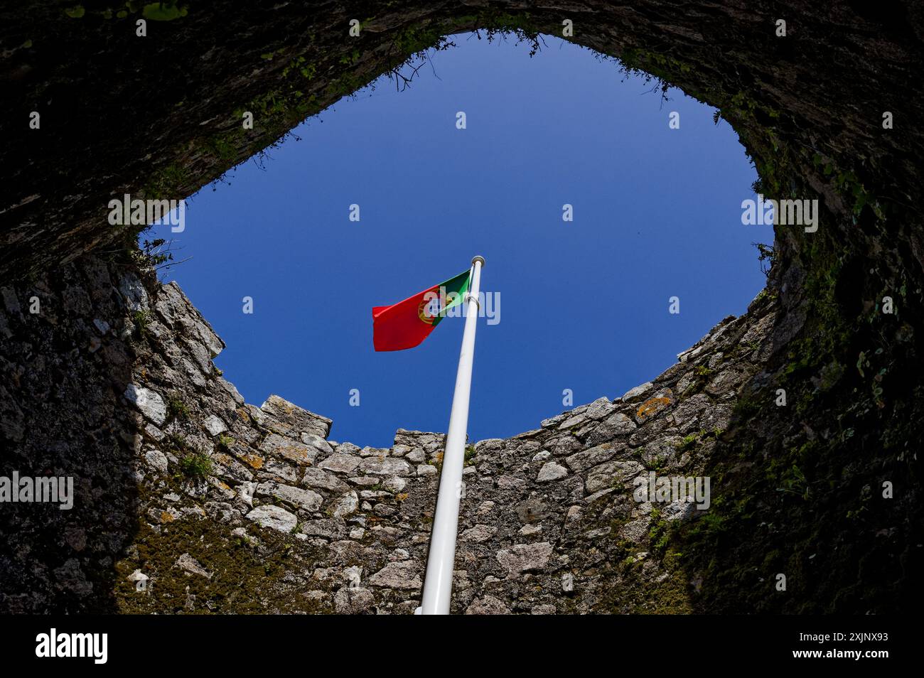 Drapeau portugais agitant au sommet d'une tour de pierre du château mauresque de Sintra, vu d'en bas avec un ciel bleu clair Banque D'Images