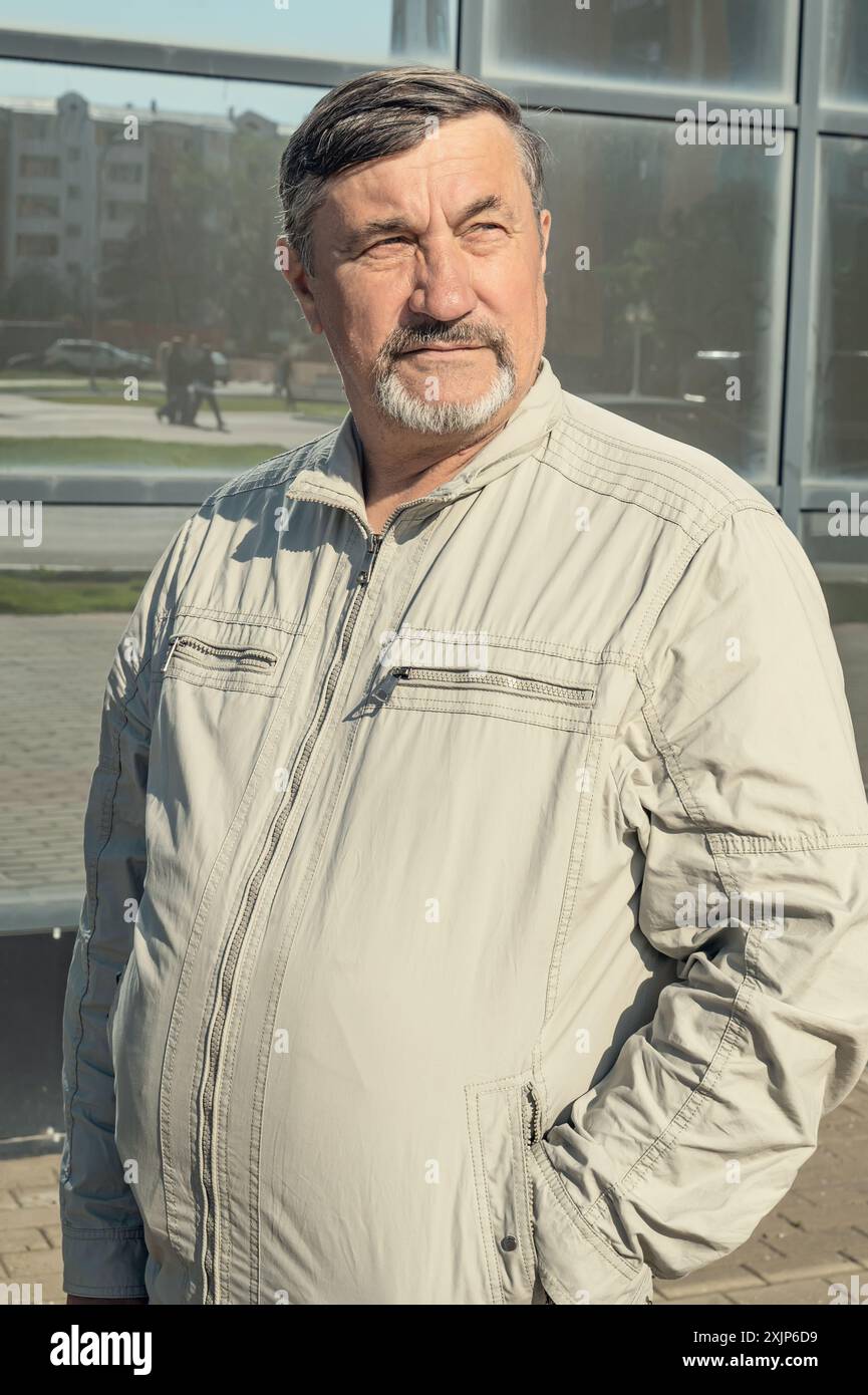 Un homme attrayant, jeune, aux cheveux gris de 70 ans avec pour toile de fond des immeubles de bureaux en verre miroir. Portrait d'une personne âgée aux cheveux gris M. Banque D'Images