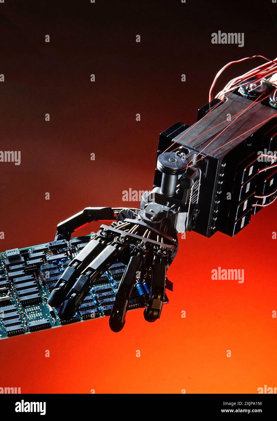 Une main robotisée, avec plusieurs joints et fils, tient une carte de circuit imprimé verte devant un fond rouge. La main est en métal noir et est en A. Banque D'Images