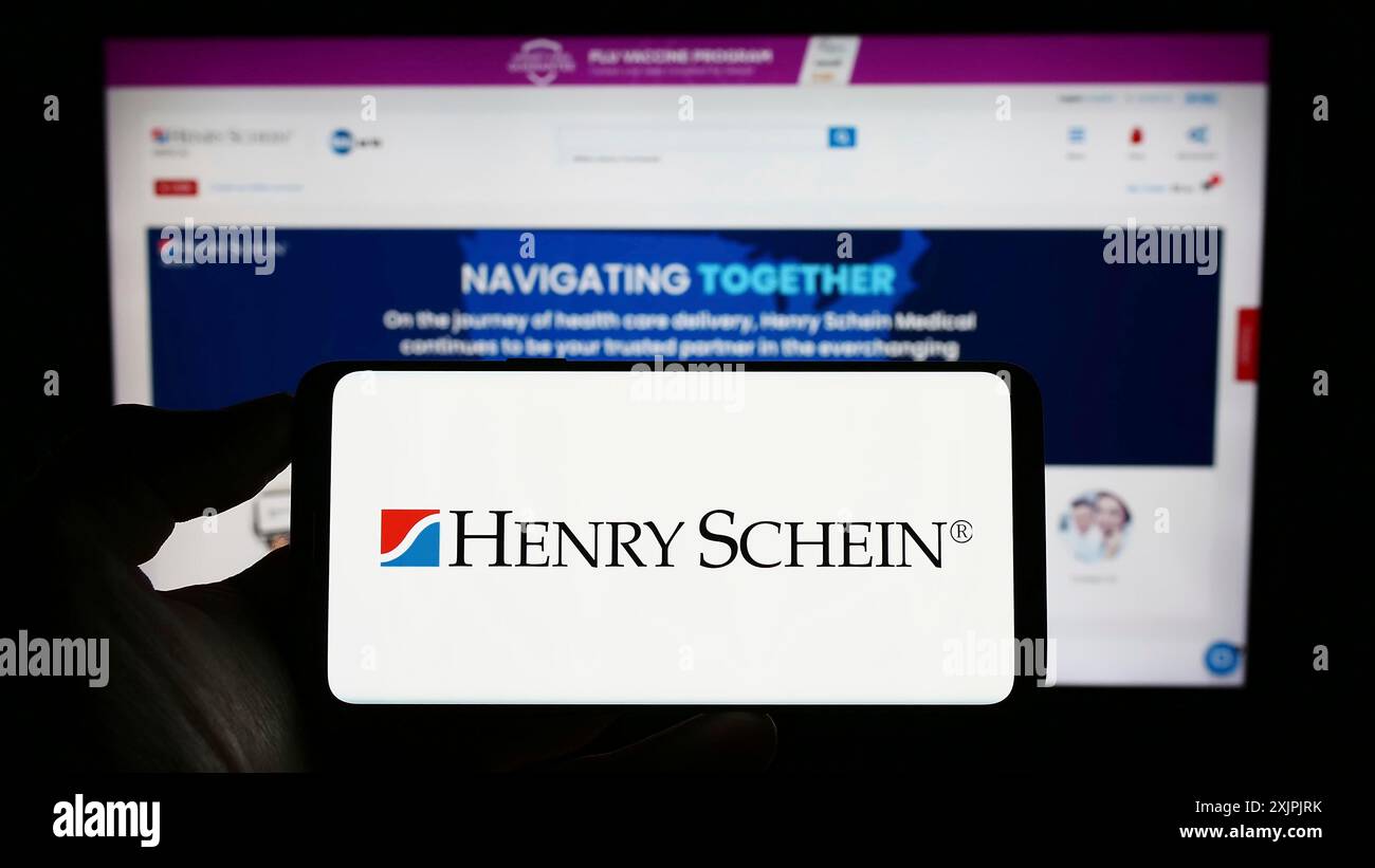 Stuttgart, Allemagne, 07-02-2023 : personne tenant un téléphone portable avec le logo de la société américaine de produits de santé Henry Schein Inc sur l'écran en face de la page Web. Banque D'Images