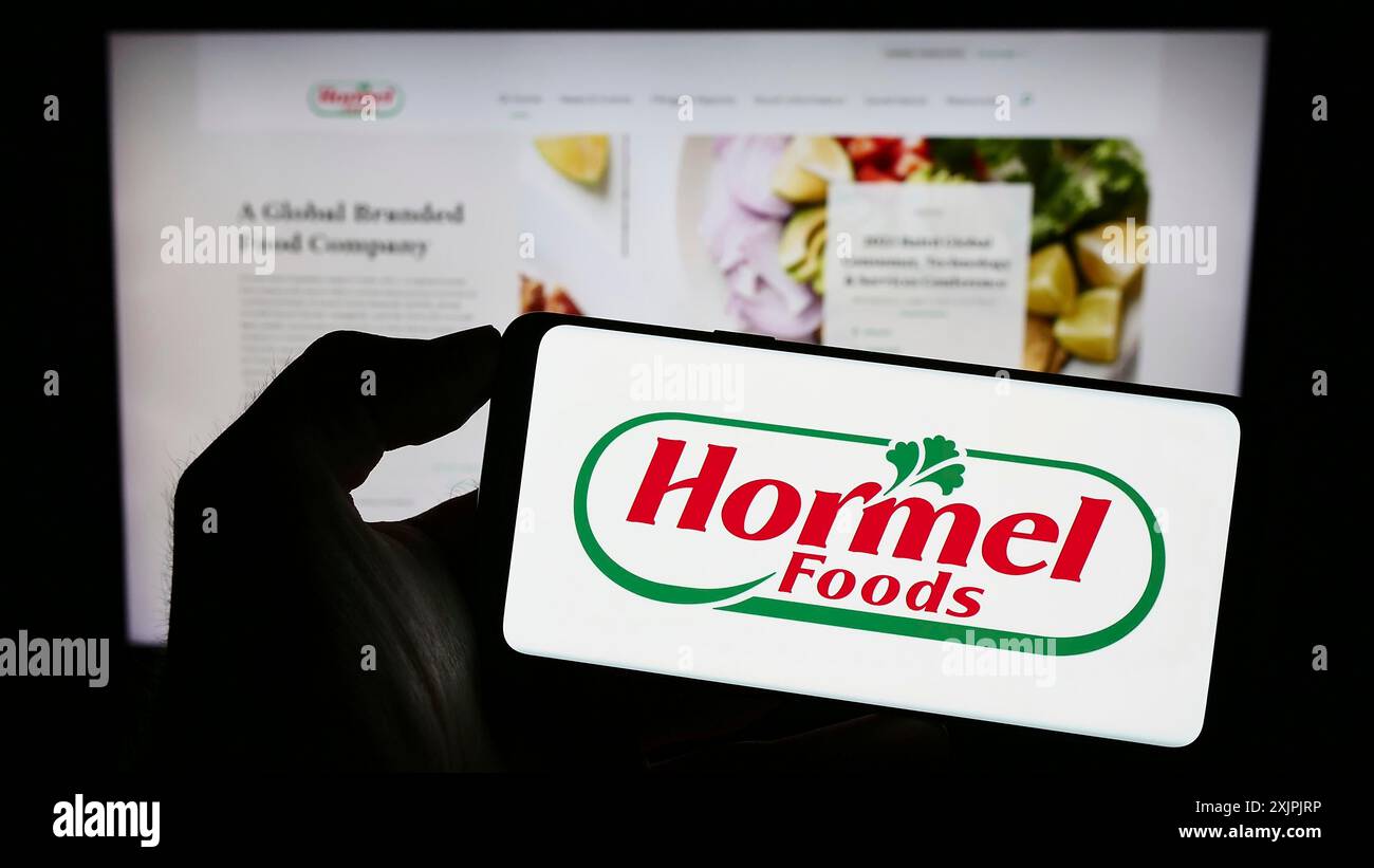 Stuttgart, Allemagne, 07-02-2023 : personne tenant un téléphone portable avec le logo de la société alimentaire américaine Hormel Foods Corporation sur l'écran devant l'entreprise Banque D'Images