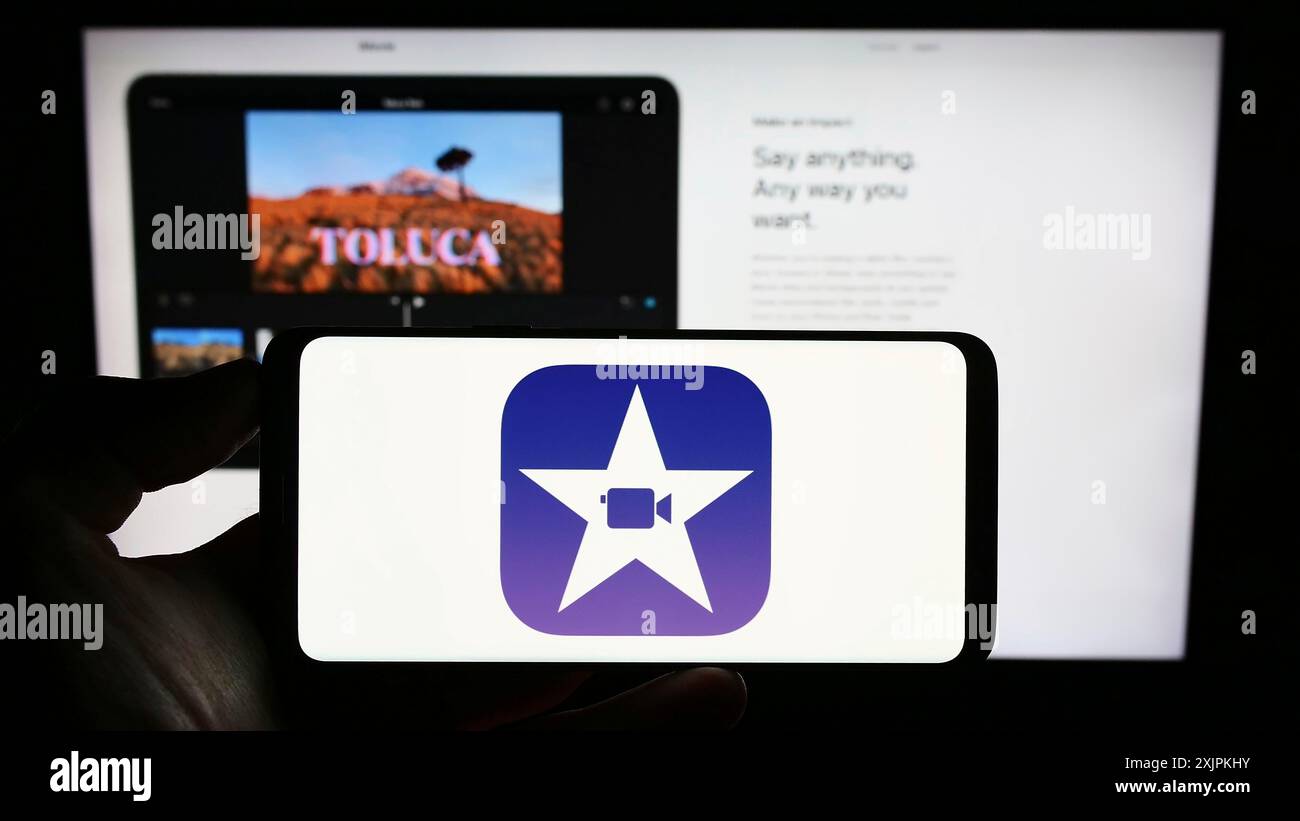 Stuttgart, Allemagne, 07-12-2023 : personne tenant un téléphone portable avec le logo du logiciel de montage vidéo iMovie (Apple Inc) sur l'écran en face de la page Web. Mise au point Banque D'Images