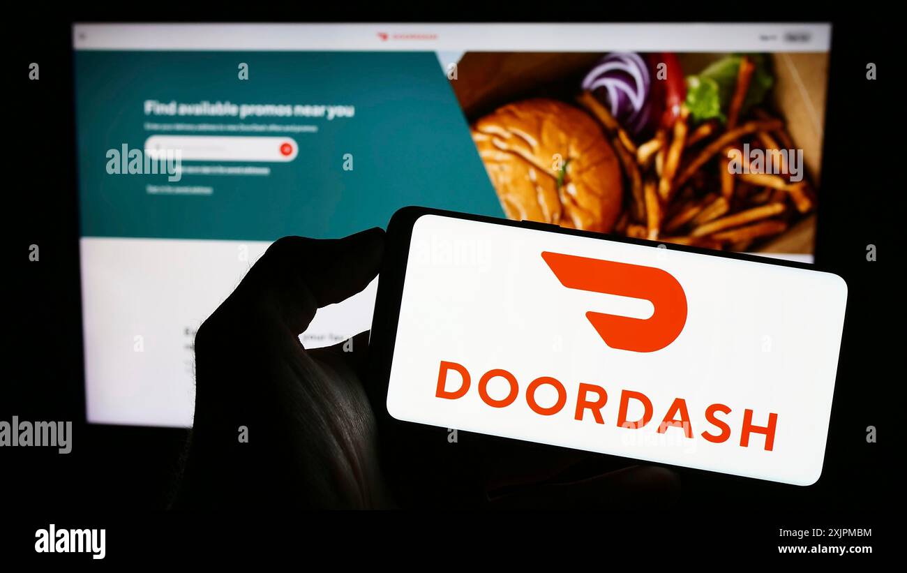 Stuttgart, Allemagne, 07-25-2023, personne tenant un téléphone portable avec le logo de la société américaine de livraison de nourriture DoorDash Inc. sur l'écran en face de la page Web de l'entreprise. Banque D'Images