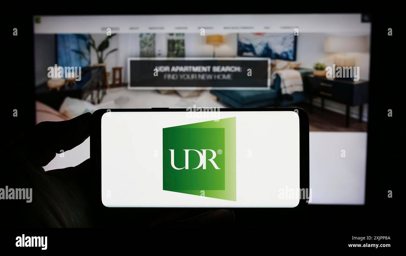 Stuttgart, Allemagne, 08-11-2023 : personne tenant un smartphone avec le logo de la société immobilière américaine UDR Inc sur l'écran devant le site Web. Concentrez-vous sur le téléphone Banque D'Images