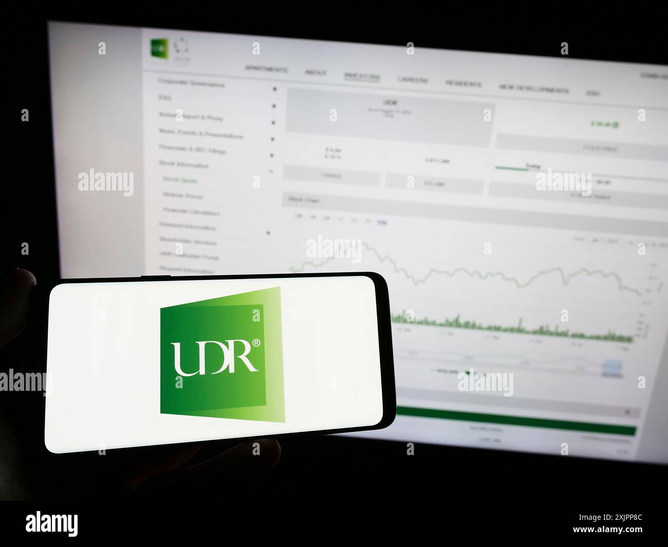 Stuttgart, Allemagne, 08-11-2023 : personne tenant un téléphone portable avec le logo de la société immobilière américaine UDR Inc sur l'écran devant le web d'affaires Banque D'Images