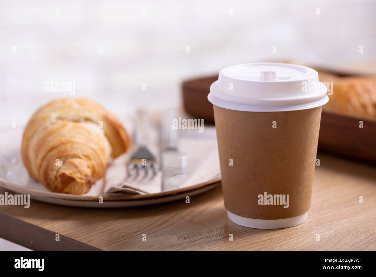 Gros plan d'un croissant au beurre classique sur une assiette blanche rustique, accompagné d'une fourchette et d'un couteau sur une serviette. Le croissant feuilleté doré Banque D'Images