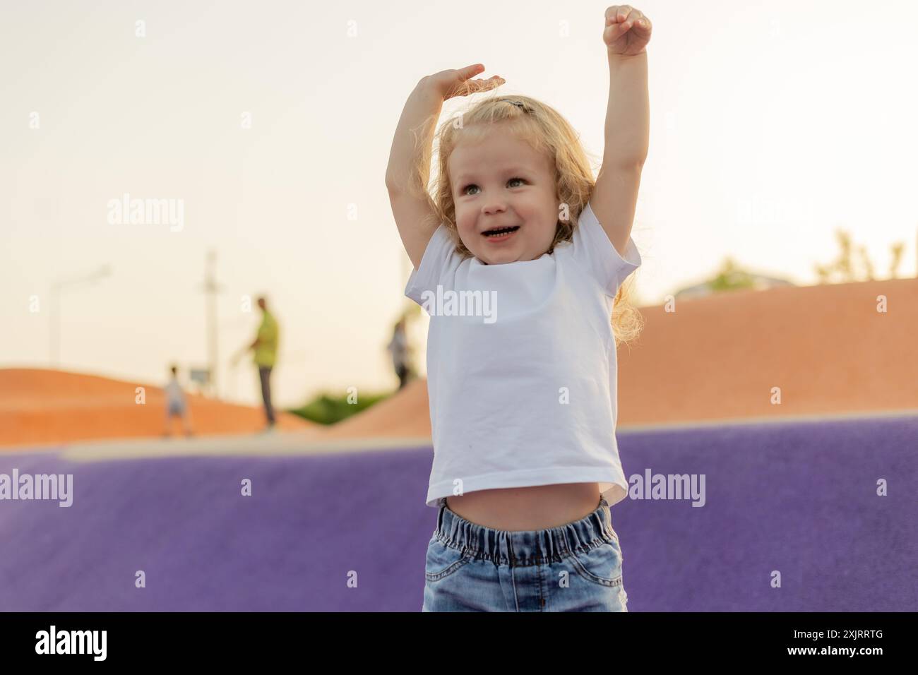 Enfant blond mignon avec les cheveux bouclés marche dans l'aire de jeux en été Banque D'Images