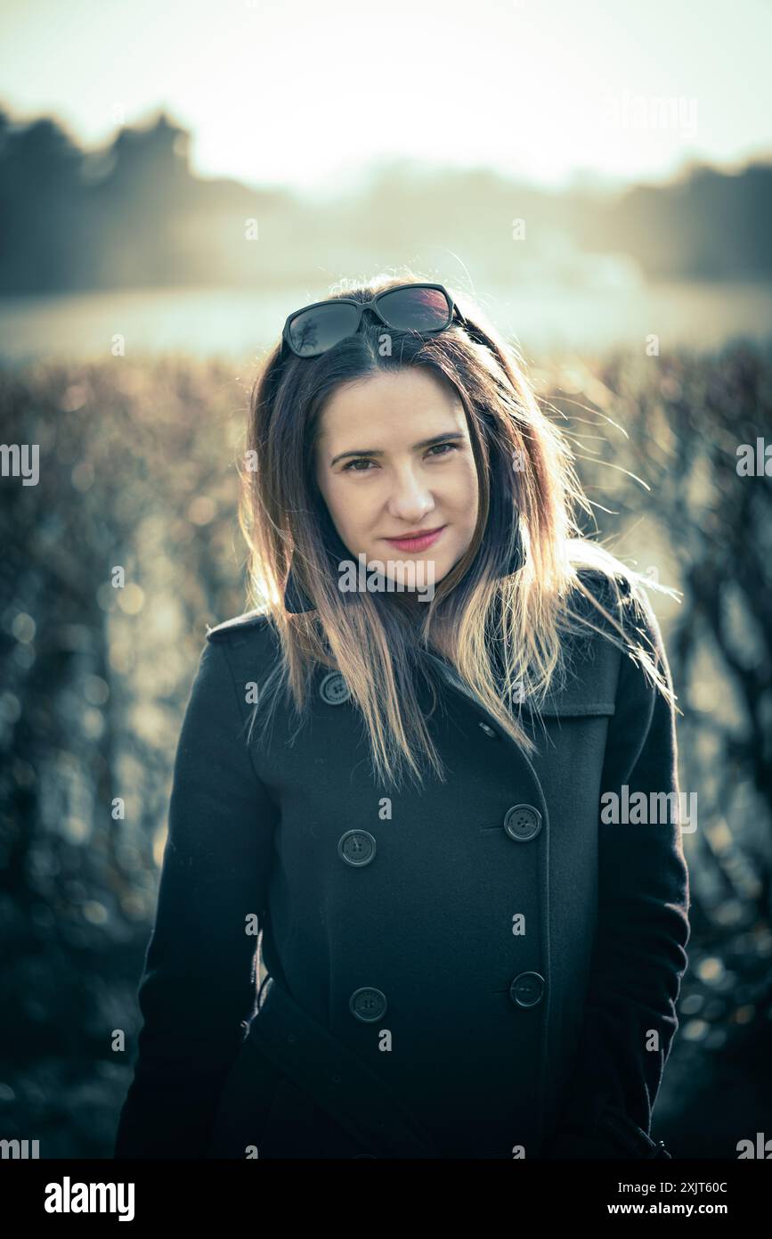 Une jeune femme, aux longs cheveux bruns et aux lunettes de soleil perchées sur la tête, regarde directement la caméra avec une expression calme et sereine. Elle porte Banque D'Images