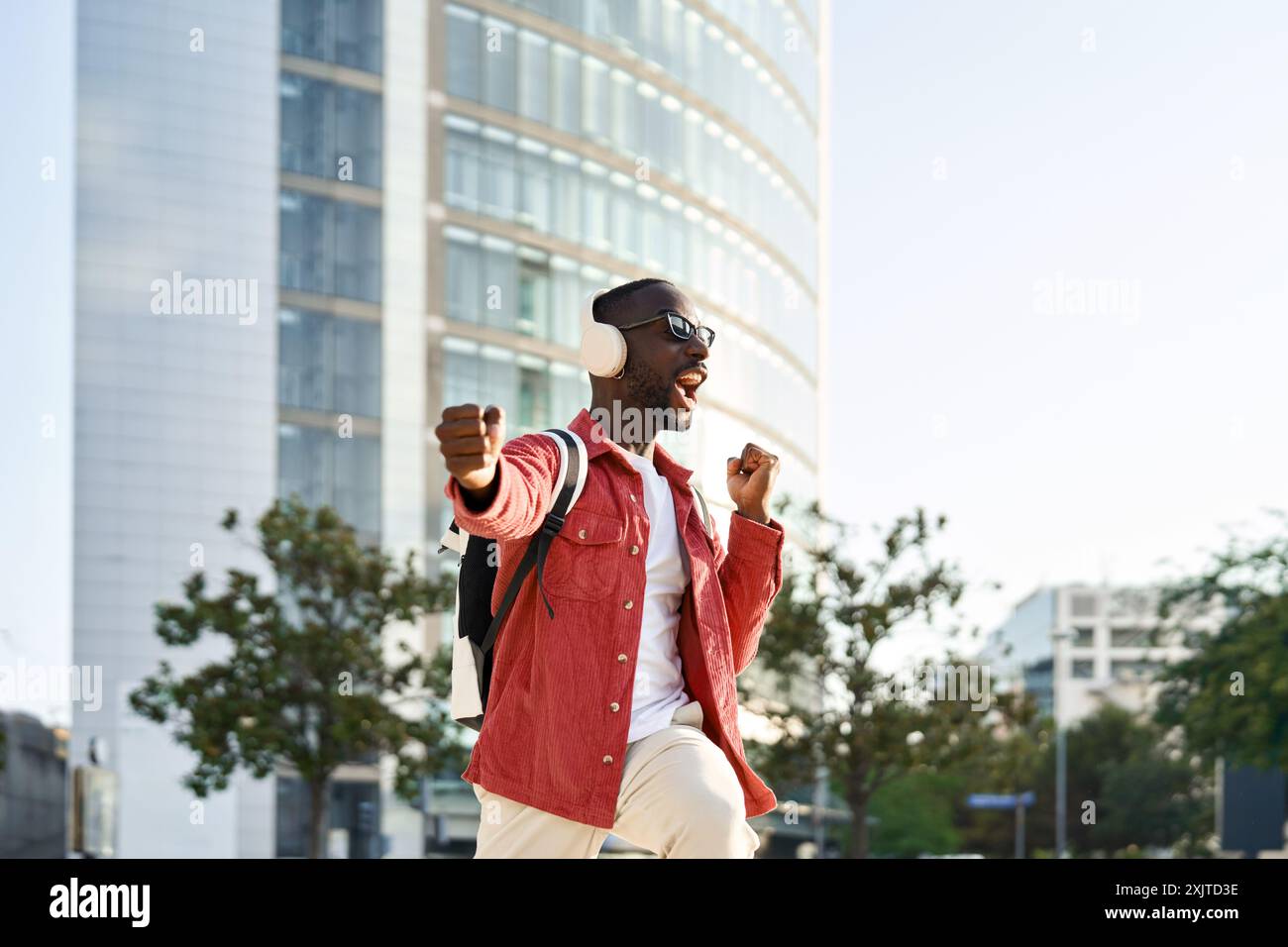 Heureux jeune homme africain excité dans des écouteurs dansant dans la rue de la ville. Banque D'Images