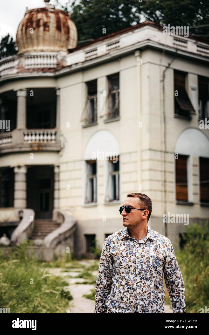 Un homme dans une chemise à motifs et des lunettes de soleil se tient devant un vieux bâtiment avec un grand dôme sur le dessus. De l'herbe verte et un sentier pavé sont dans le Forward Banque D'Images