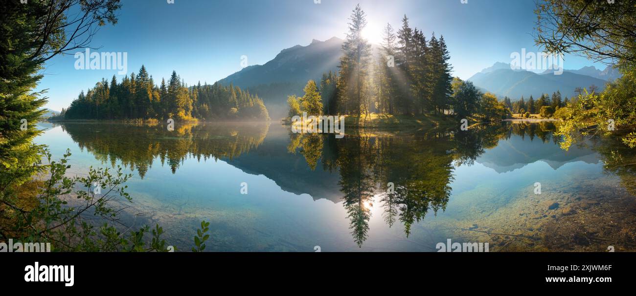 Paysage de lac peint avec des montagnes et des arbres reflétés dans l'eau. Un paysage panoramique idyllique avec de beaux rayons de soleil Banque D'Images