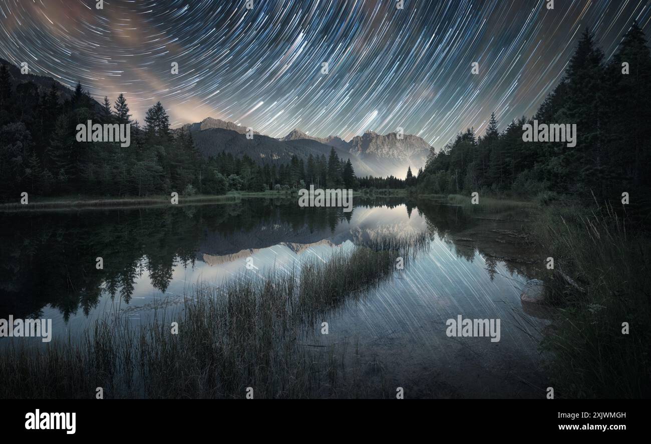 Des sentiers étoilés sur des paysages majestueux peints reflétés dans un lac, avec des montagnes en arrière-plan. Prise de vue nature astrophotographique longue exposition Banque D'Images