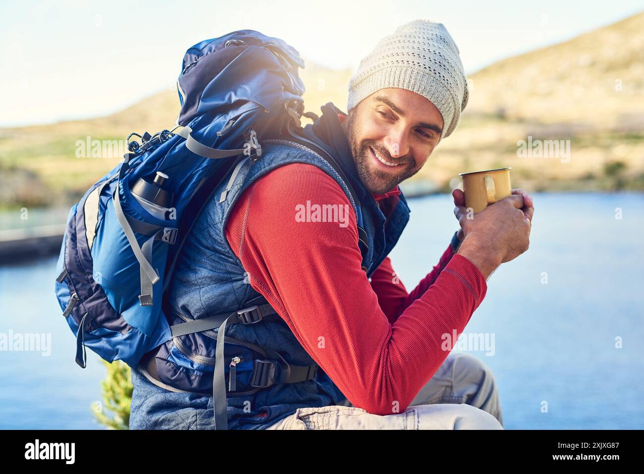 Randonnée, heureux et homme par le lac avec café le matin pour l'aventure, trekking et camping sur le voyage. Voyage, montagne et personne à l'extérieur pour le bien-être Banque D'Images